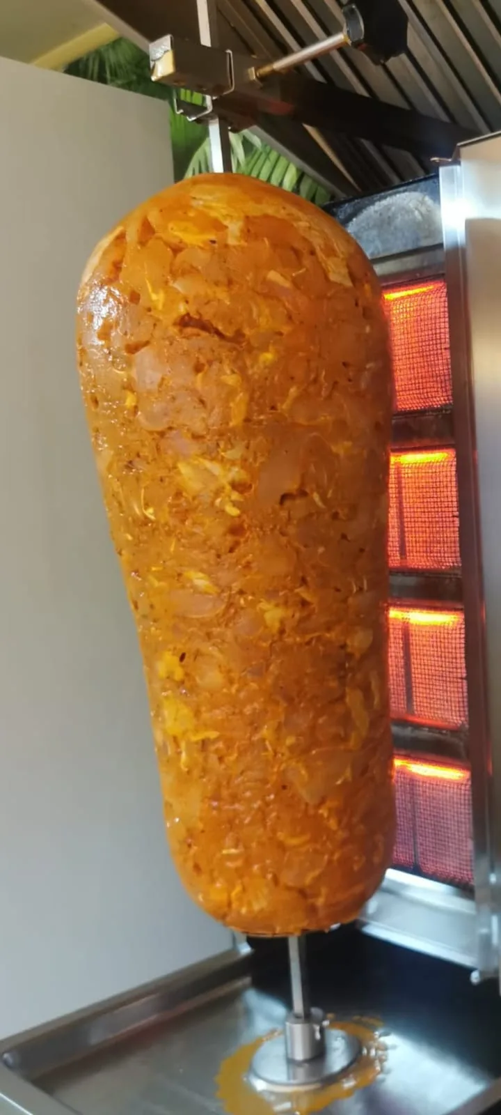 Arkasında yanan ızgaralarla döner ocağında baharatlı tavuk döner.